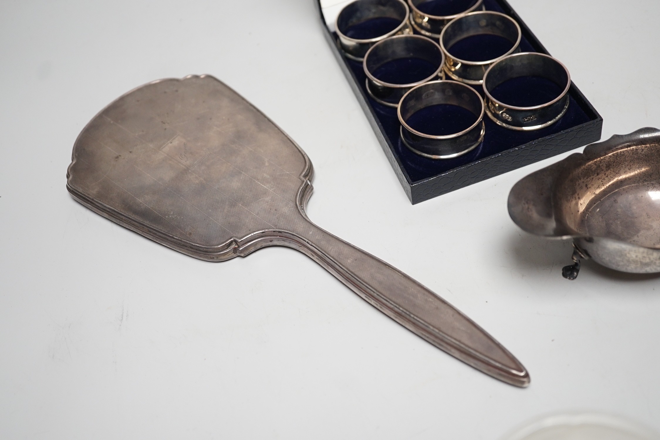 A set of six modern silver napkin rings, a George V silver sauceboat and a silver mounted hand mirror.